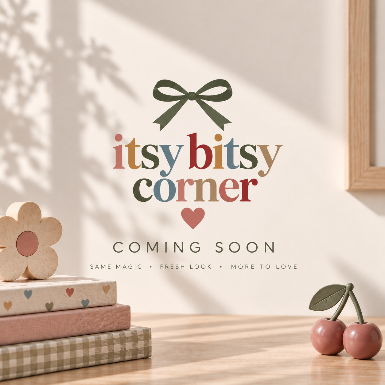 Itsy Bitsy Corner. Coming soon. Same magic, fresh look, more to love. An olive ribbon above colorful lettering, with wooden flowers, stacked fabrics, and pink cherries in the sunshine.